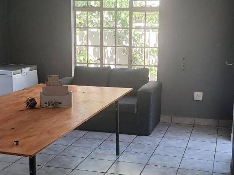 A living area featuring grey tiled flooring, a multi-pane window, and a crystal chandelier, providing a functional space with potential for cosmetic updates.