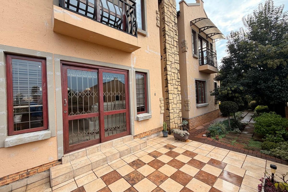 Rear exterior view of the cluster home featuring a tiled patio, stone-clad chimney detail, and upper-level balconies with wrought iron railings.