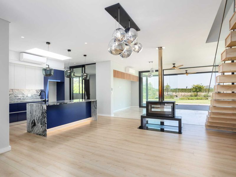Spacious open-plan living area featuring a modern kitchen with stone island, a striking central fireplace, and a timber staircase leading to the upper level.