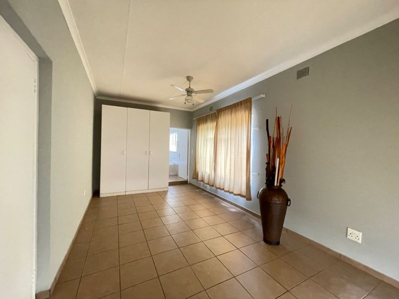 A spacious bedroom featuring neutral wall tones, tiled flooring, built-in cupboards, and a ceiling fan, offering a clean and functional living space.