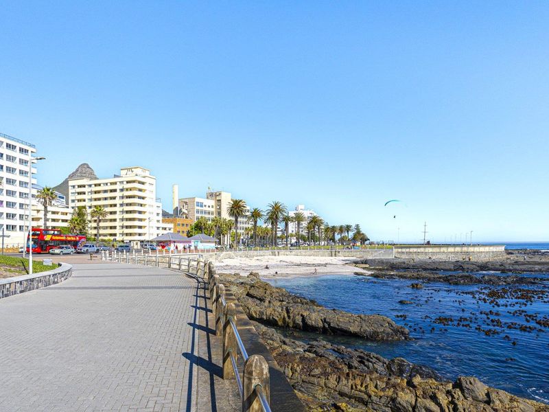Scenic coastal view featuring a paved promenade, rocky shoreline, and surrounding apartment buildings along the beachfront.