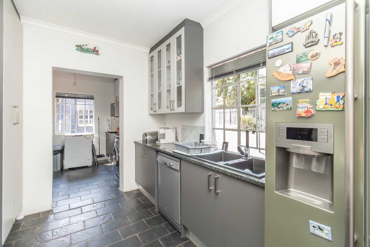 A functional kitchen featuring grey cabinetry, stone-look countertops, a double sink, and tiled flooring, with an adjacent scullery area visible through the doorway.