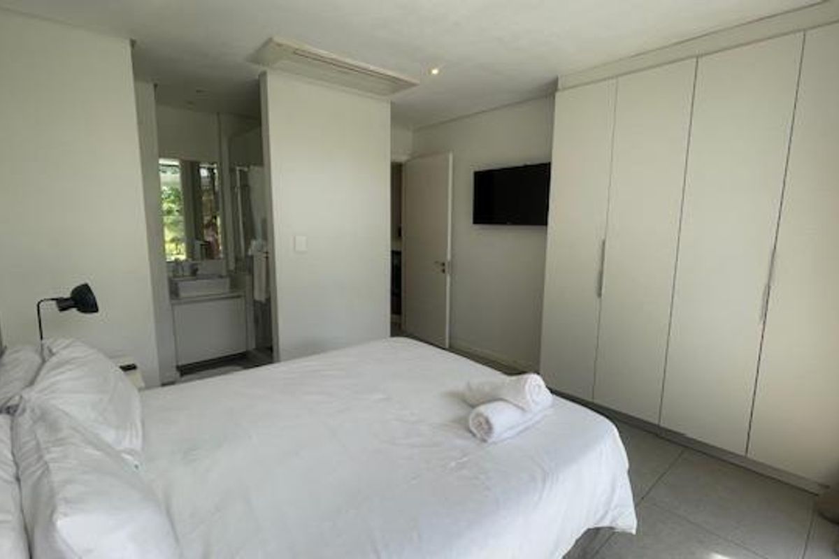 Modern bedroom featuring built-in cupboards, tiled flooring, recessed lighting, and an integrated en-suite bathroom with a vanity.