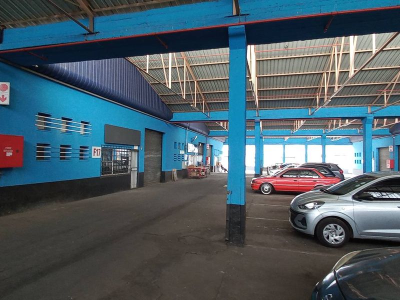 Spacious industrial garage facility featuring high ceilings with exposed steel trusses, roller shutter access, and durable asphalt flooring, suitable for vehicle storage or workshop use.