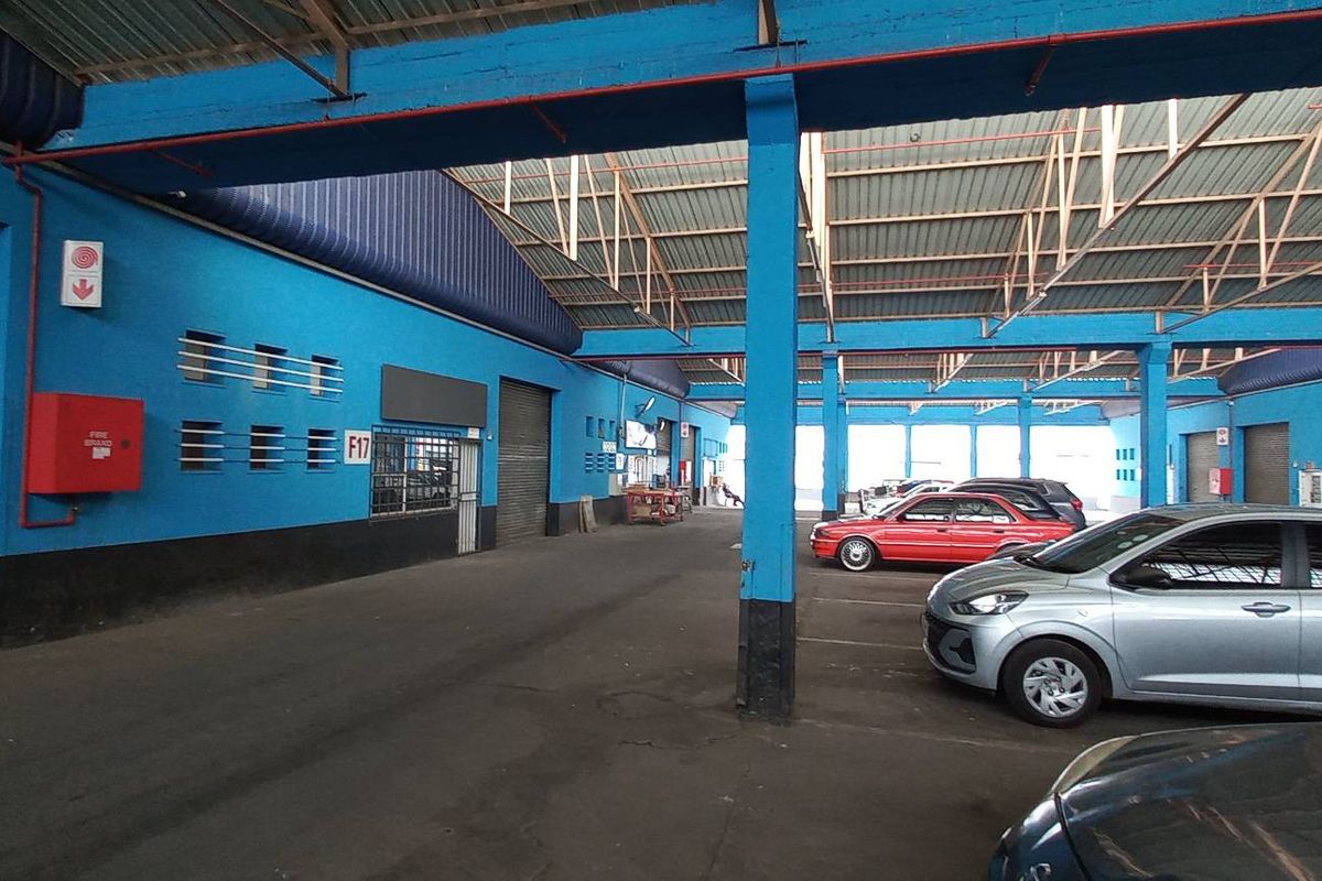Spacious industrial garage facility featuring high ceilings with exposed steel trusses, roller shutter access, and durable asphalt flooring, suitable for vehicle storage or workshop use.
