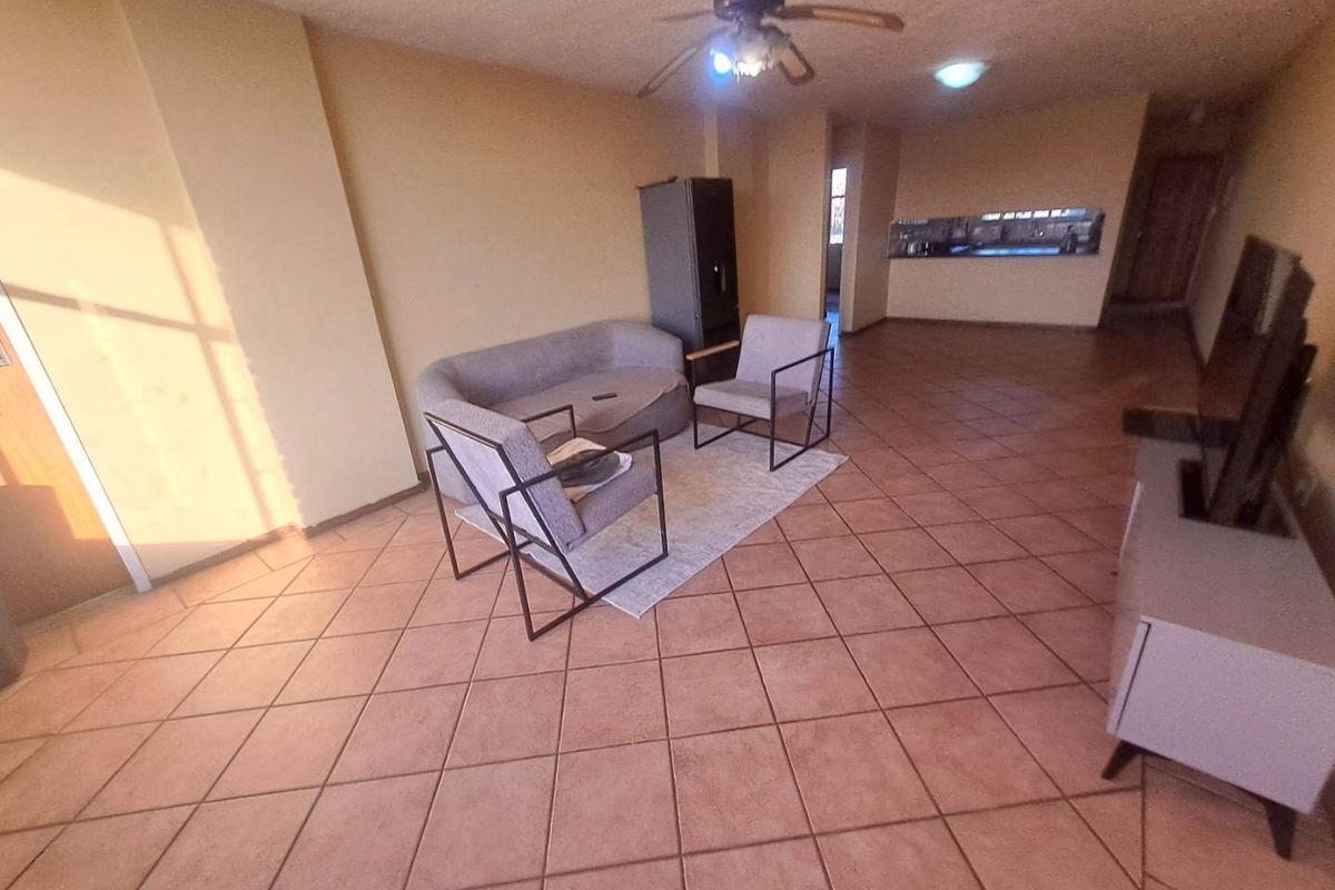 Open-plan living area featuring tiled flooring, a ceiling fan, and a pass-through window connecting to the kitchen space.