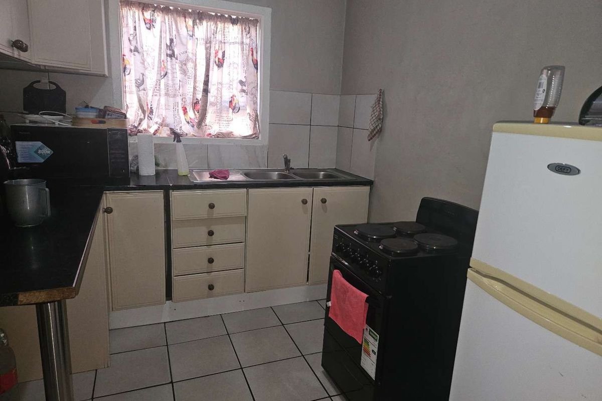 A functional kitchen featuring laminate cabinetry, double bowl sink, tiled splashback, and ceramic floor tiles, offering potential for cosmetic updates.
