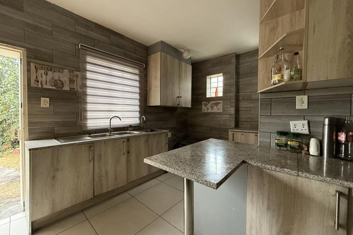 A functional kitchen featuring wood-look cabinetry, granite countertops, a double sink, and tiled splashbacks with direct access to the exterior.