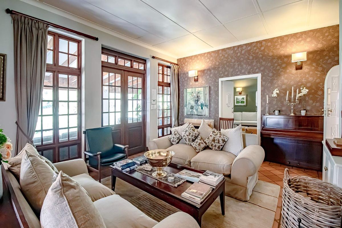 A cozy living room featuring terracotta floor tiles, patterned wallpaper, and multiple timber-framed glass doors providing access to the outdoor area.