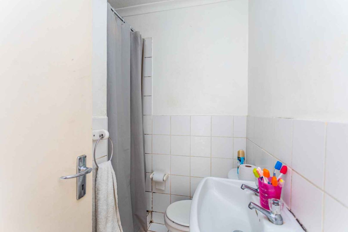 A compact bathroom featuring a pedestal sink, toilet, and a shower area with a curtain, requiring some cosmetic updates to the tiling and fixtures.