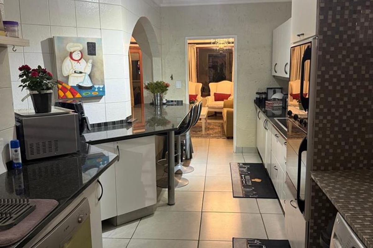 A functional kitchen featuring granite countertops, built-in cabinetry, and a breakfast bar, with an open archway leading into the adjacent living area.