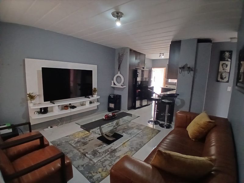 An open-plan living area featuring a built-in media console, tiled flooring, and a breakfast bar connecting to the kitchen space.