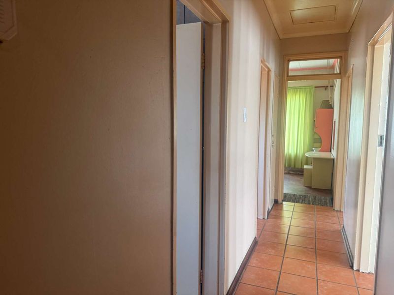 A narrow interior hallway featuring terracotta-style floor tiles and multiple doorways leading to adjacent rooms.