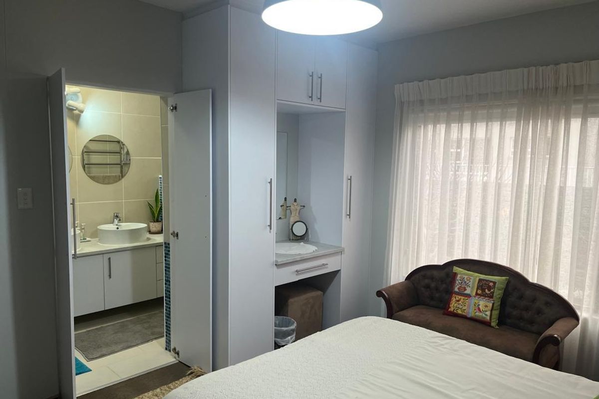 A well-maintained bedroom featuring built-in cupboards with an integrated vanity station and direct access to an en-suite bathroom.