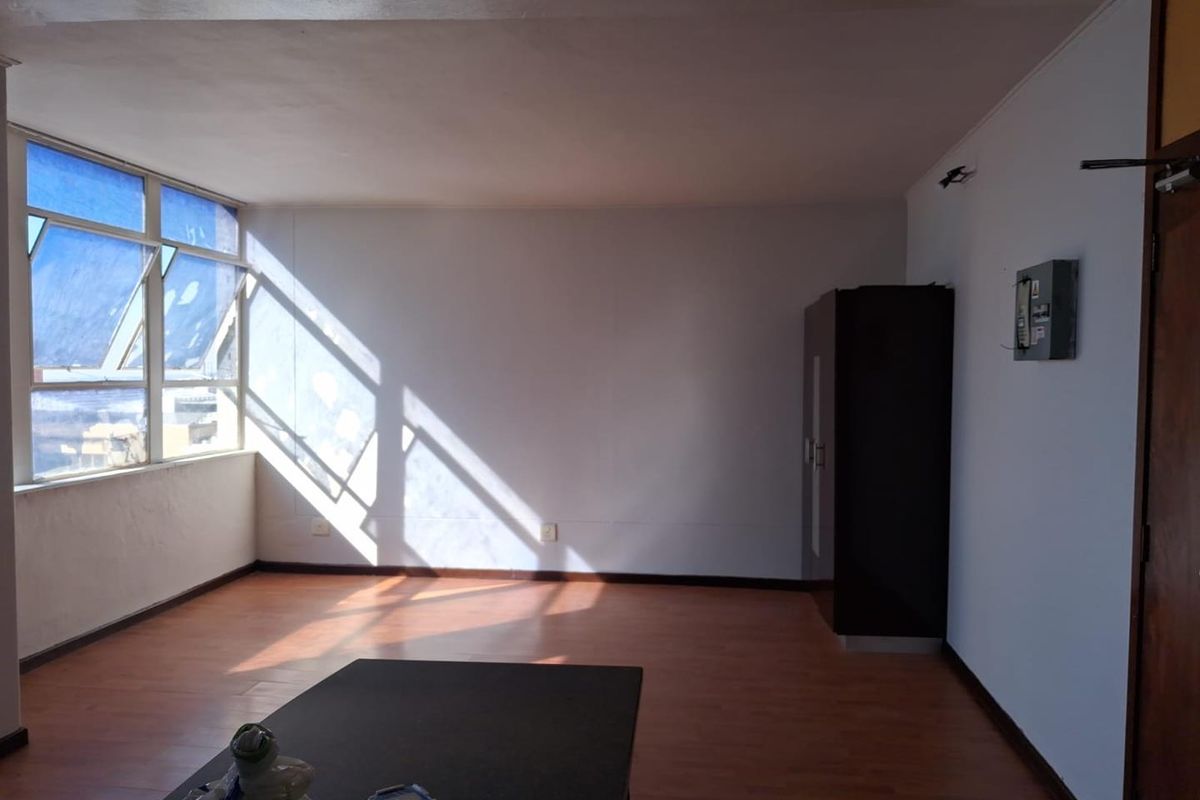 A spacious, sunlit living area featuring laminate flooring and large windows, offering a blank canvas for interior design and renovation.