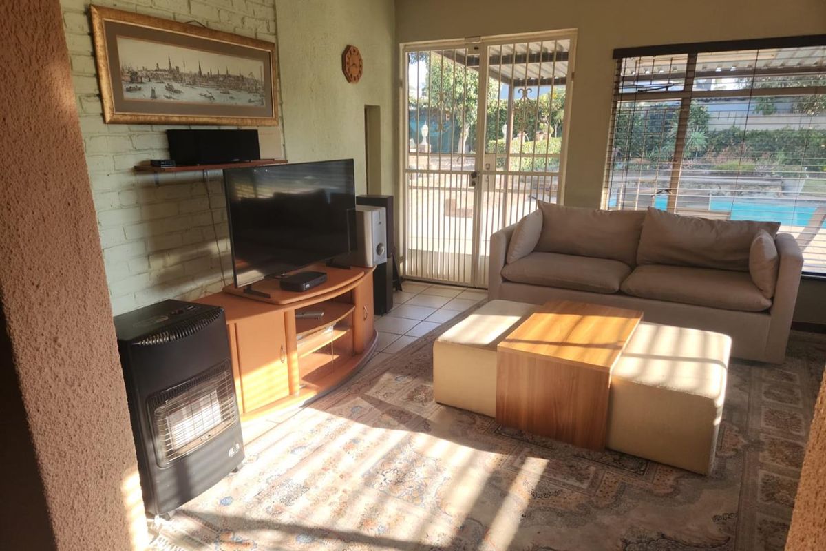 A sunlit living room featuring painted brick walls, tiled flooring, and direct access to the outdoor pool area through a secure sliding door.