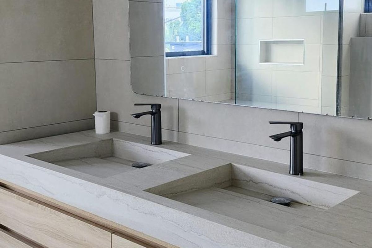 Modern bathroom featuring a double vanity with integrated stone sinks, matte black faucets, light wood cabinetry, and a large wall-mounted mirror.