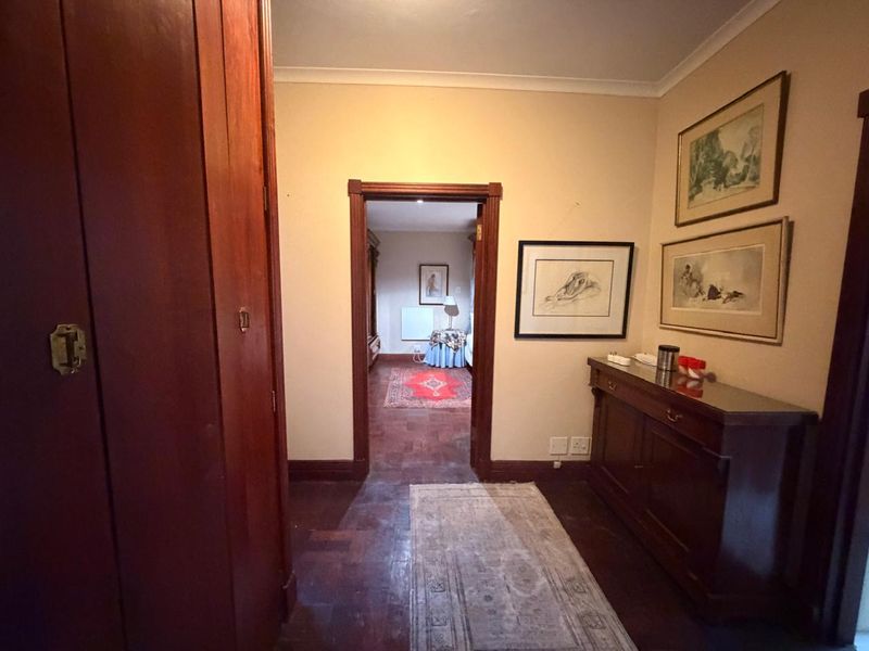 A traditional hallway featuring dark parquet flooring, built-in wooden cabinetry, and coved ceilings, providing access to an adjoining bedroom space.