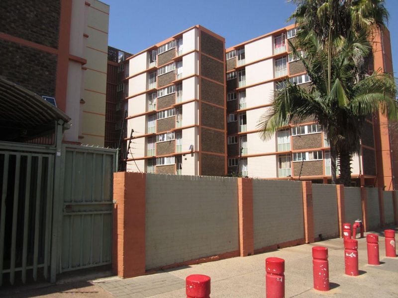 Exterior view of a multi-story apartment complex featuring a perimeter wall, security gate, and street-level bollards.