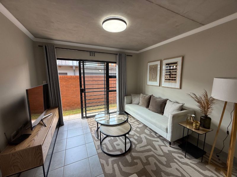 A well-maintained living room featuring tiled floors, an exposed concrete ceiling, and a sliding glass door providing access to the outdoor area.
