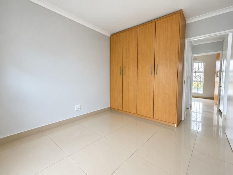 A bright, empty bedroom featuring neutral tiled flooring, smooth walls, and ample built-in wooden cupboards, offering a clean and versatile living space.