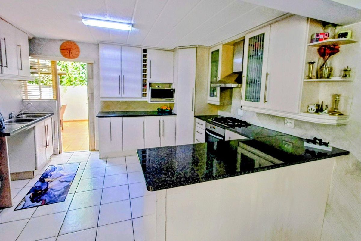 Functional kitchen featuring granite countertops, built-in oven, gas hob, extractor fan, and ample cabinetry, with direct access to an outdoor patio area.