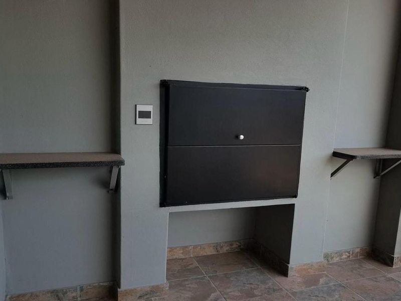 A clean, covered balcony area featuring a built-in braai and stone-look floor tiles, providing a functional outdoor entertainment space.