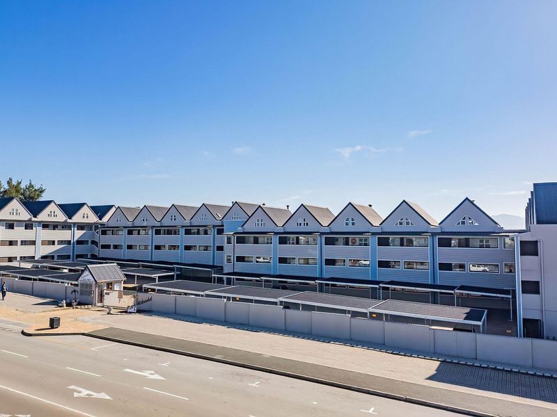 An aerial view of a multi-story apartment complex featuring gabled roof architecture, extensive covered parking facilities, and a secure perimeter wall.