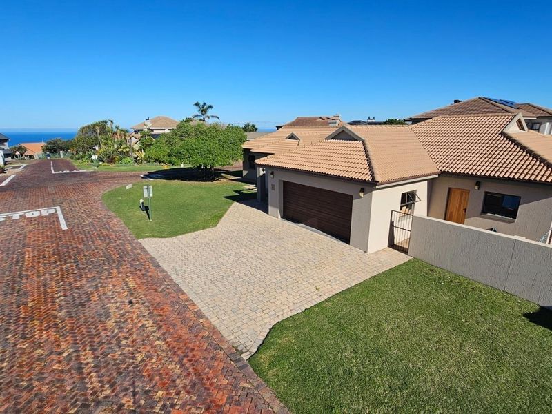 Aerial view of a residential property featuring a tiled roof, paved driveway, double garage, and surrounding landscaped garden in a quiet street.