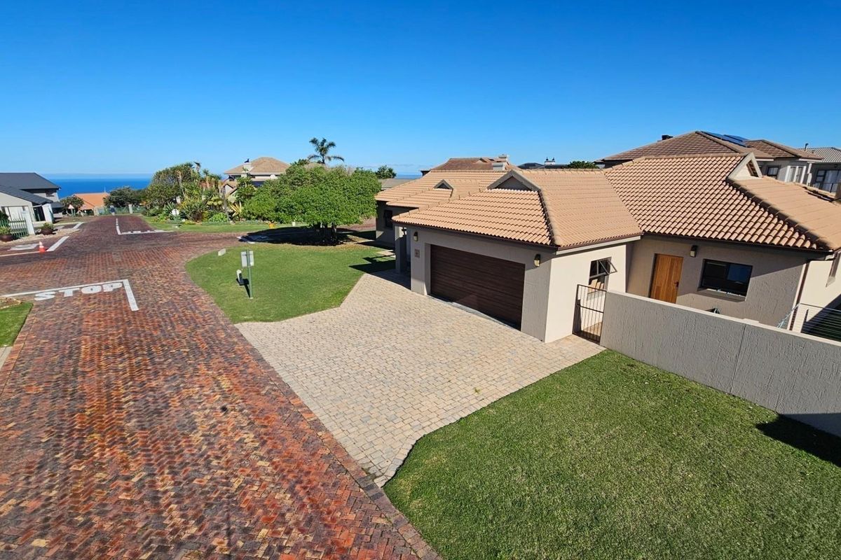 Aerial view of a residential property featuring a tiled roof, paved driveway, double garage, and surrounding landscaped garden in a quiet street.