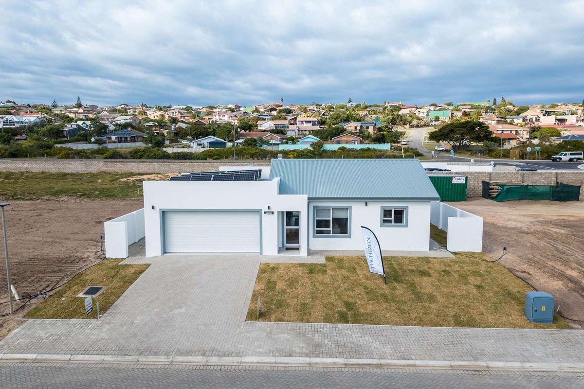 Aerial view of a modern single-story house featuring a paved driveway, double garage, and roof-mounted solar panels in a residential neighborhood.