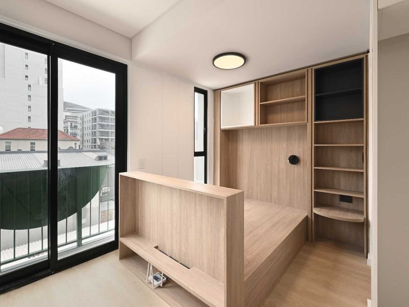 Modern bedroom featuring a custom built-in bed frame with integrated shelving and large sliding glass doors leading to a balcony.