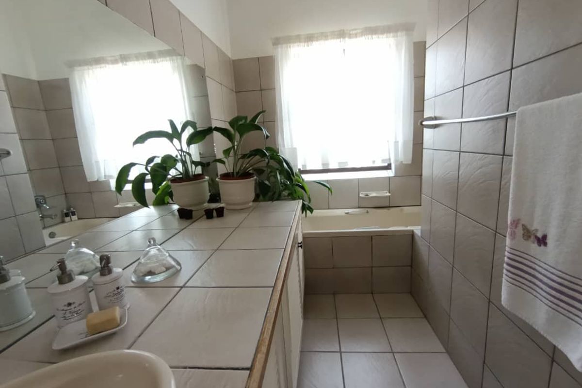 A functional bathroom featuring a tiled vanity with integrated basin, large wall mirror, and a built-in bathtub with tiled surround.