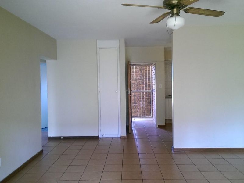 An empty living area featuring tiled flooring, a ceiling fan, and a built-in storage cupboard, with access to an exterior security gate.
