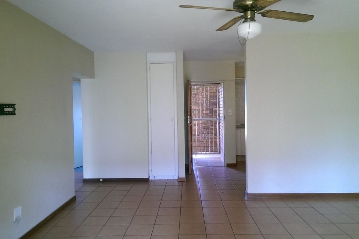 An empty living area featuring tiled flooring, a ceiling fan, and a built-in storage cupboard, with access to an exterior security gate.