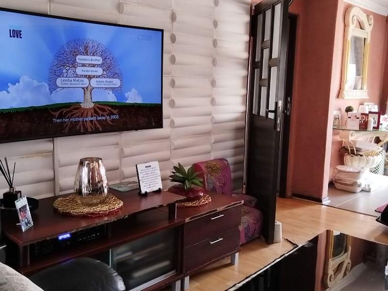 A living room featuring textured wall paneling, decorative ceiling cornices, and laminate flooring, leading into an adjacent hallway area.