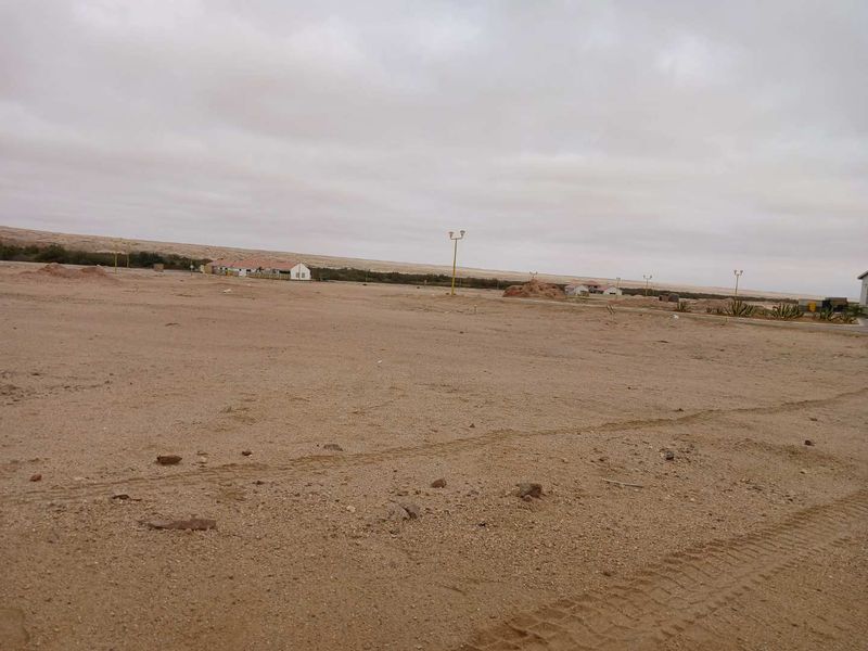 A vacant residential plot of land featuring sandy terrain and existing street lighting infrastructure in a developing area.