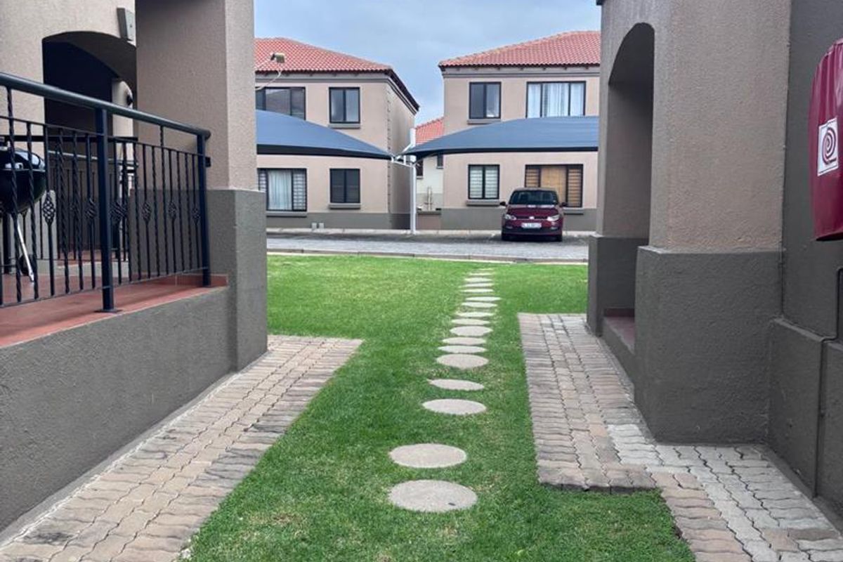 A view of the communal garden area between townhouse units, featuring paved walkways, stepping stones, and covered patio spaces.
