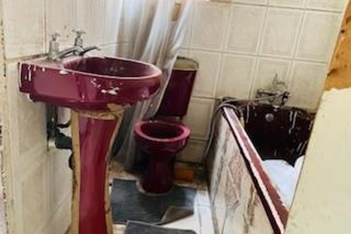A dated bathroom featuring a burgundy pedestal basin, matching toilet, and bathtub with wall-mounted shower mixer and tiled surround.
