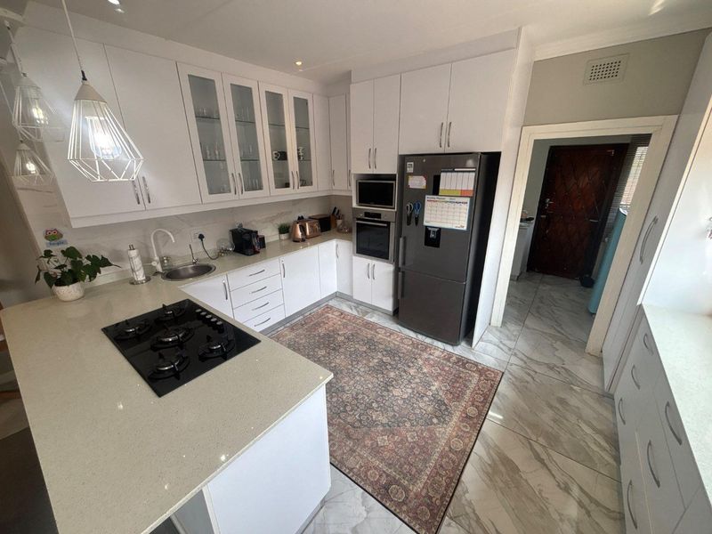 Modern kitchen featuring white cabinetry, stone countertops, integrated gas hob, built-in oven, and microwave, complemented by stylish tiled flooring.