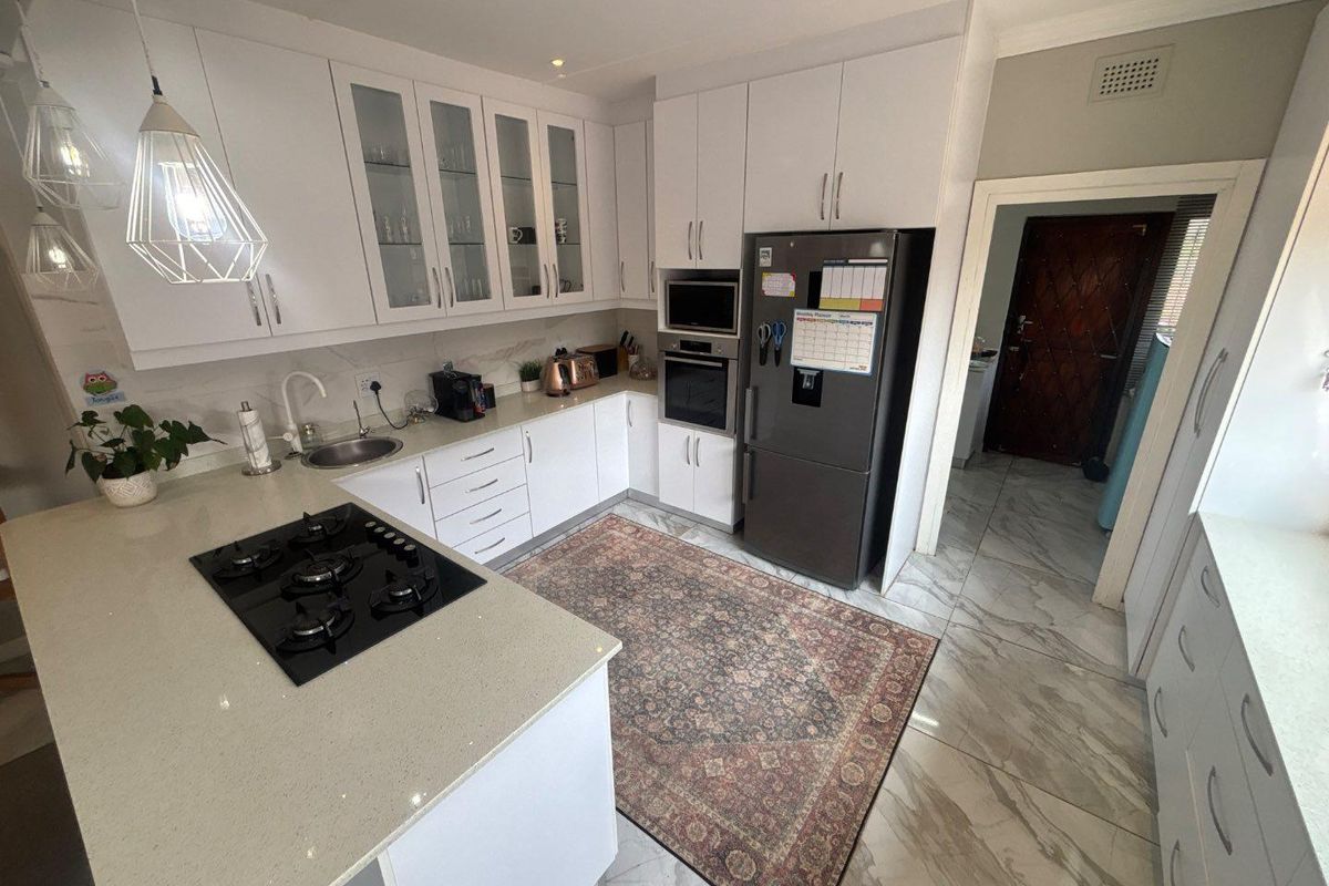 Modern kitchen featuring white cabinetry, stone countertops, integrated gas hob, built-in oven, and microwave, complemented by stylish tiled flooring.