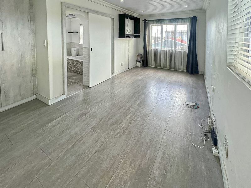 A spacious, empty bedroom featuring modern grey tiled flooring, built-in cabinetry, and an en-suite bathroom access point.