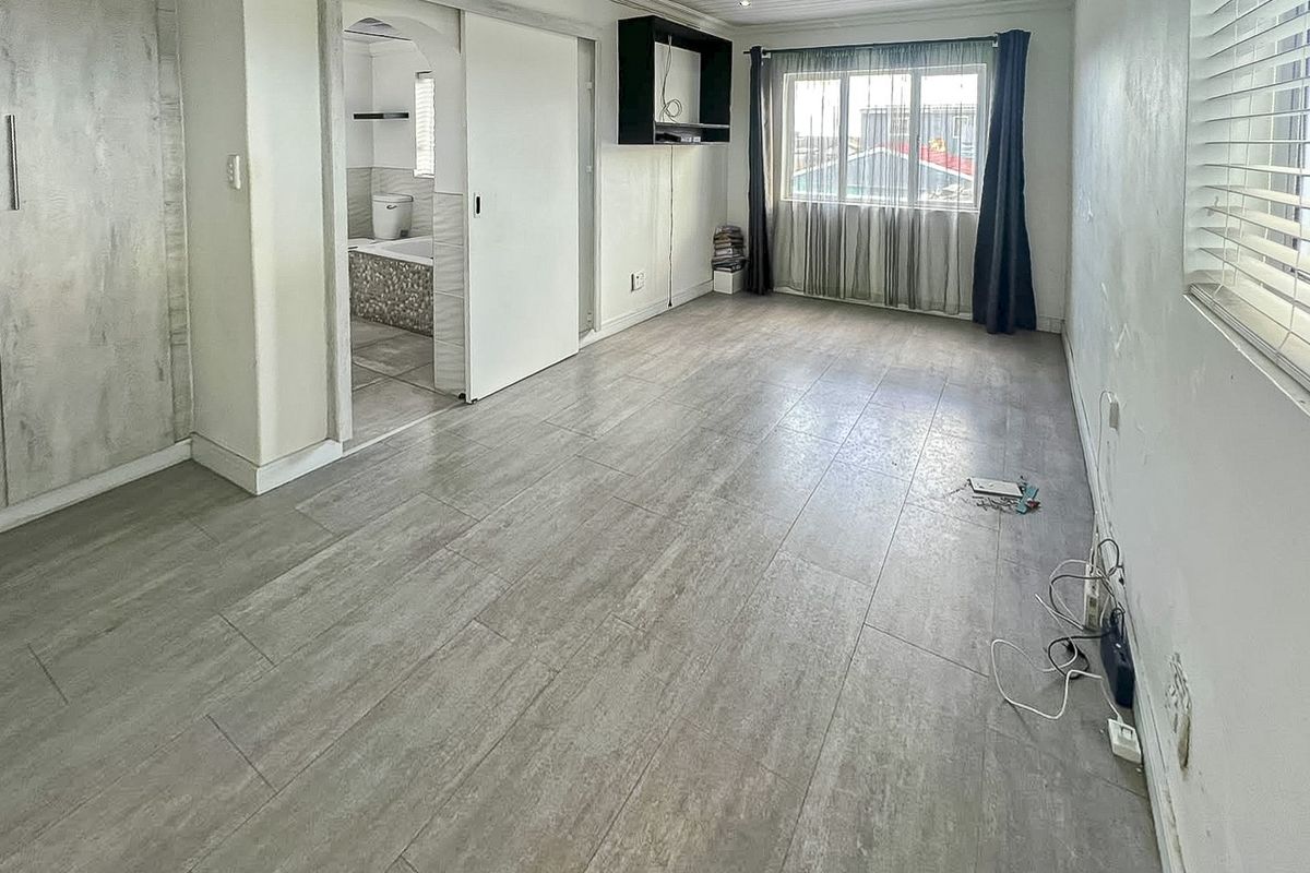 A spacious, empty bedroom featuring modern grey tiled flooring, built-in cabinetry, and an en-suite bathroom access point.