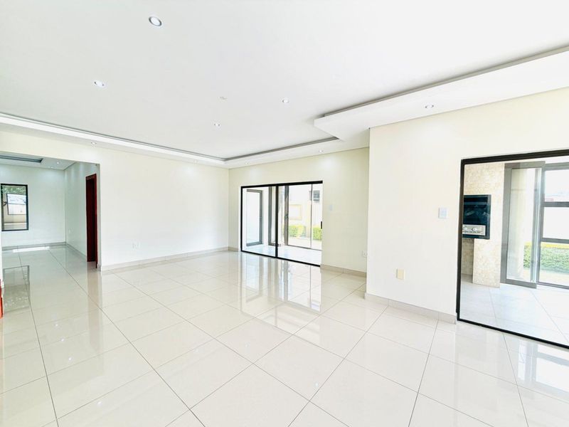 Spacious open-plan living area featuring polished porcelain tiles, recessed downlighting, bulkhead ceilings, and large sliding doors leading to an outdoor area with a built-in braai.