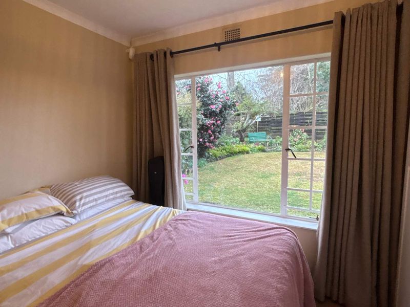 A cozy bedroom featuring a large window with garden views and built-in cupboard storage.