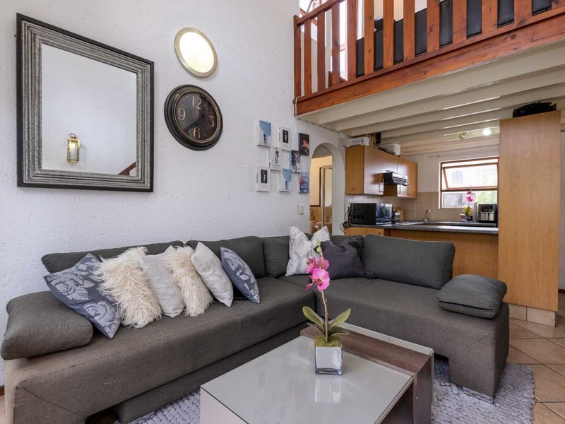Open-plan living area featuring a mezzanine level with wooden railing, exposed ceiling beams, and an integrated kitchen with wooden cabinetry.