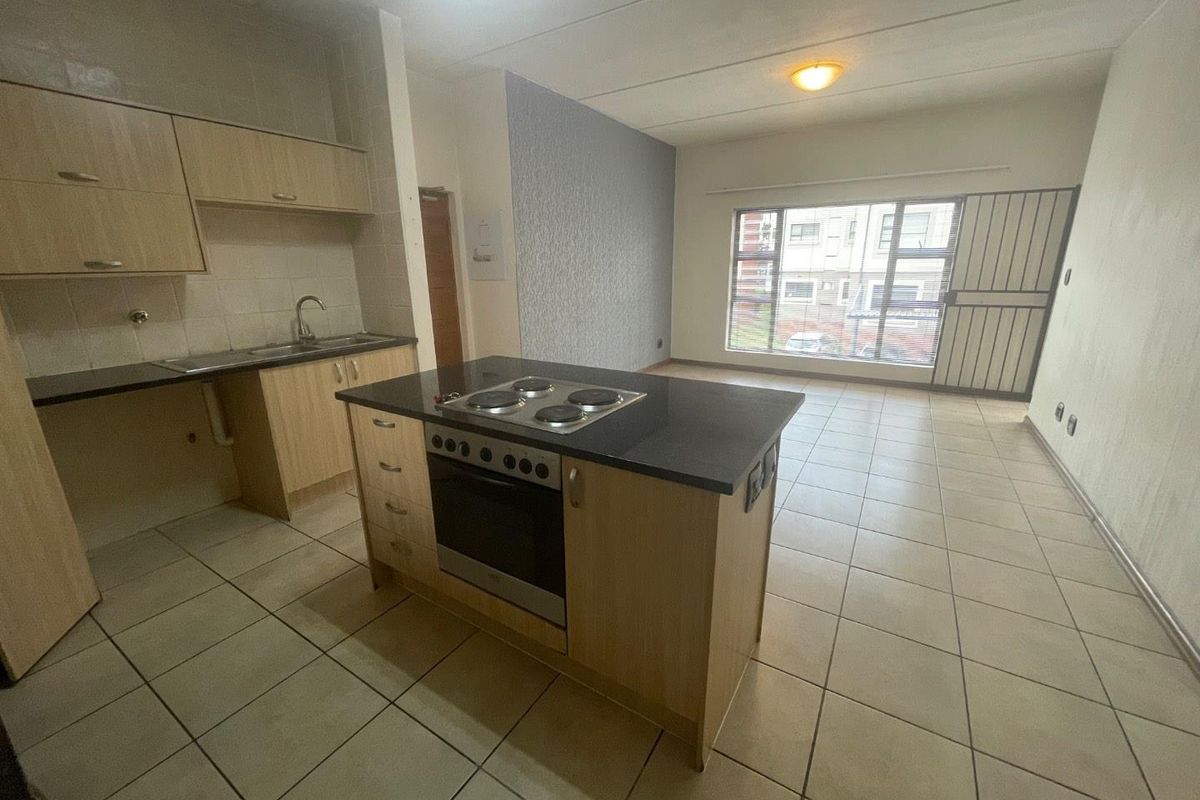 Spacious open-plan kitchen and living area featuring a central island with built-in oven and hob, tiled flooring, and large windows for natural light.