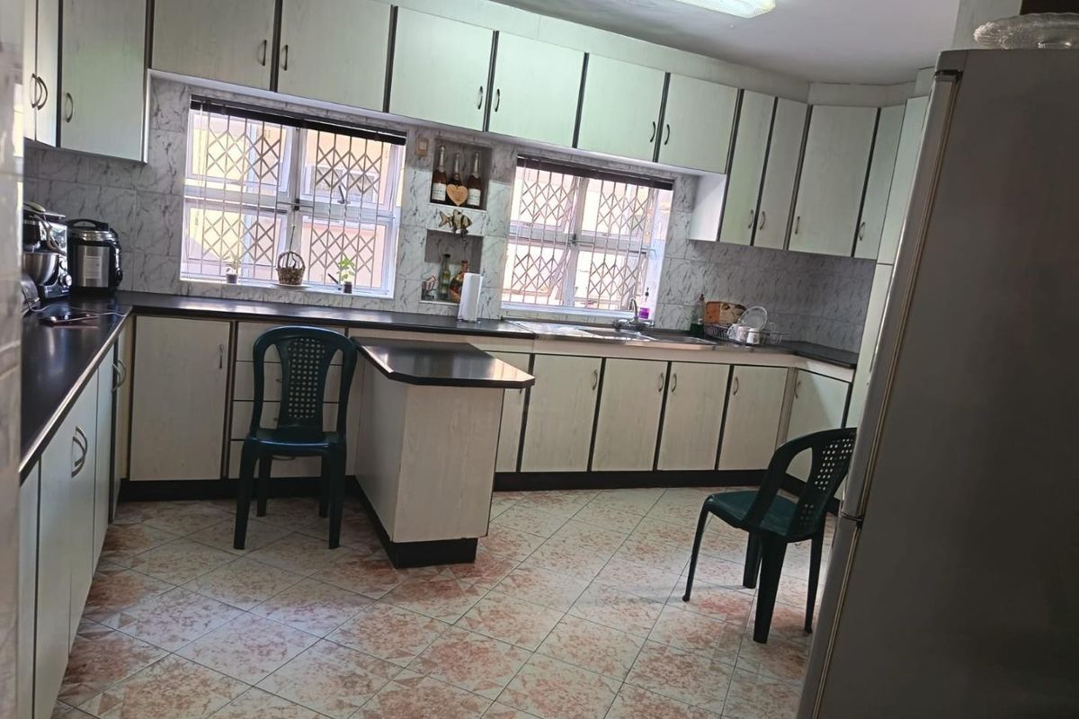A functional kitchen featuring extensive laminate cabinetry, laminate countertops, a stainless steel sink, and tiled flooring with security bars on the windows.