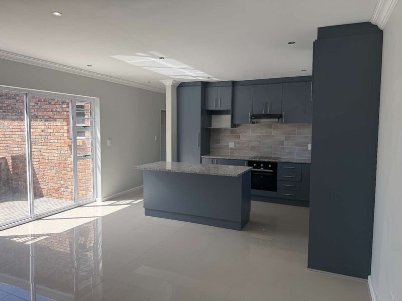 Modern open-plan kitchen featuring dark cabinetry, granite countertops, a central island, and sleek tiled flooring, seamlessly connected to an outdoor patio area.