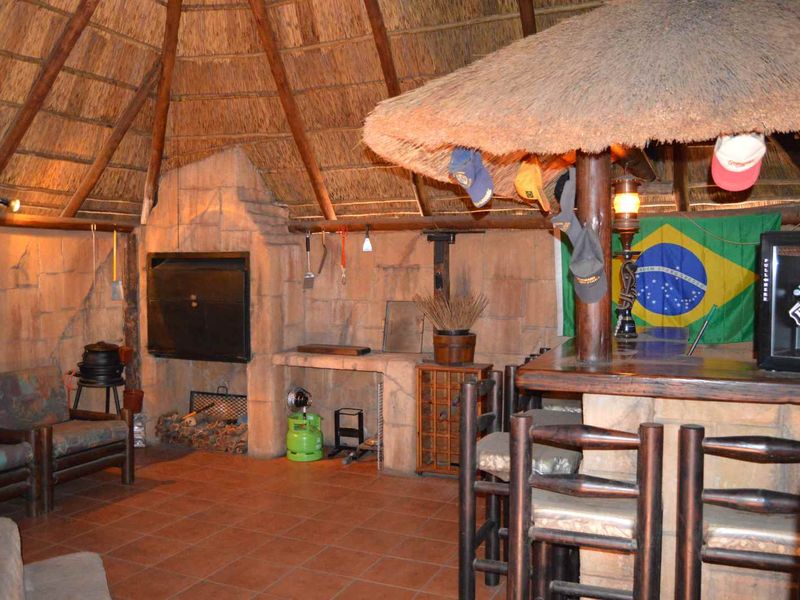 Rustic entertainment area featuring a thatched roof, built-in braai, and a custom bar counter with stone masonry finishes.